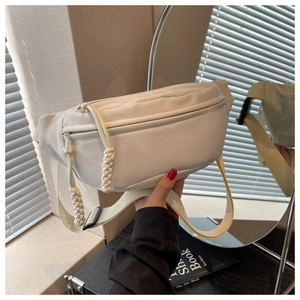 Close-up of beige canvas crossbody bag with woven zipper pull held in a trendy setting