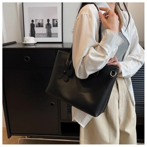 Detail of a large black tote bag featuring white contrast stitching and flower charm