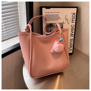 Close-up of pink tote bag with smooth faux leather texture and plush peach charm