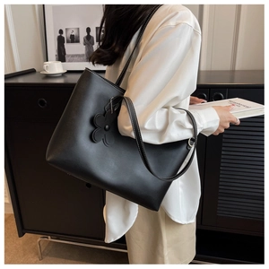 Detail of black tote bag with white contrast stitching and a floral charm on the strap