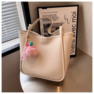 Detail view of large cream tote bag on metal table with cute peach plush pendant