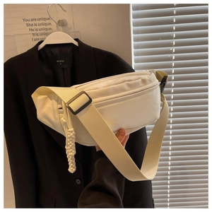 Detail of off-white canvas chest bag featuring adjustable strap and woven rope charm