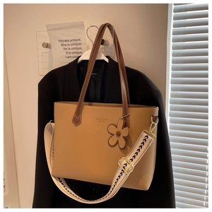 Detail of khaki tote bag with wide wavy strap and flower charm on black blazer display