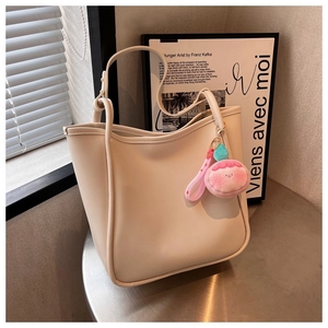 Detail of off-white leather tote bag featuring a cute pink peach plush pendant on side