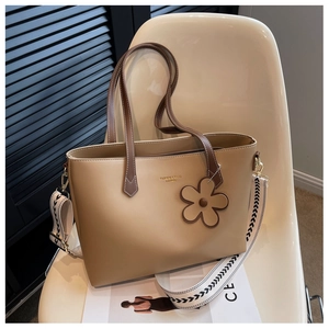 Detail of khaki tote bag with ethnic woven strap and floral charm on a chair