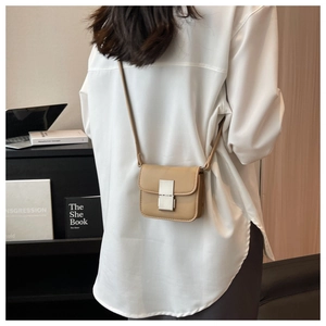 Mini beige leather crossbody bag with silver square lock worn by a model in a modern room