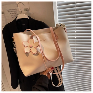 Detail view of cream leather tote bag with wide geometric strap and floral pendant
