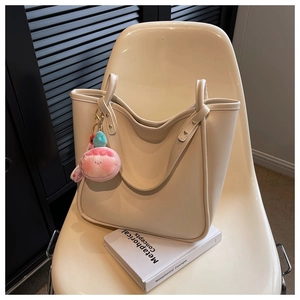 Detail of off-white tote bag with gold rivets and pink plush pendant on a chair