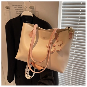 Detail of a large cream tote bag with pink handles, floral charm, and a wide woven strap