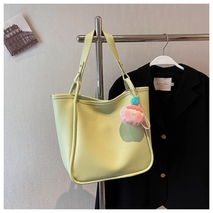 Detail view of a light green PU leather tote bag featuring a pink plush ball charm