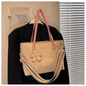 Detail of beige tote bag with pink handle, floral charm, and geometric wide strap