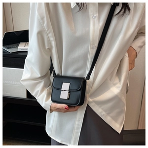 Detail of a black mini square leather crossbody bag with silver clasp worn by a model