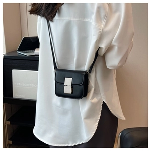 Detail shot of a mini black crossbody bag worn on a white shirt showing scale and matte texture
