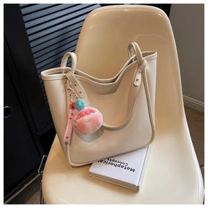 Detail of cream large tote bag with pink plush charm on an artistic chair