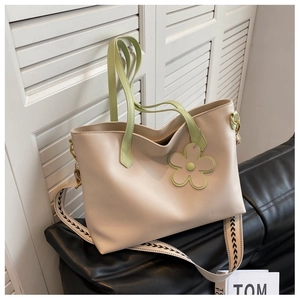 Close-up of cream leather tote bag with green handle and patterned wide strap detail