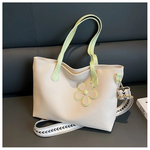 Detail of cream tote bag featuring green handles and a black and white geometric strap