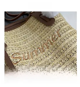 Detail of straw tote bag showing Summer embroidery, leather handle and fluffy pompom charm