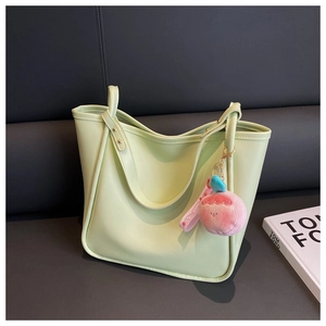 Close-up of light green faux leather tote bag with a pink peach plush charm on a sofa