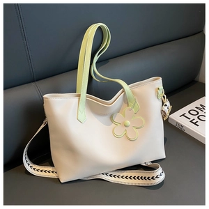 Detail of beige tote bag with green strap and floral charm on a grey textured bench
