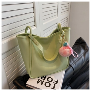 Macro detail of a light green leather tote bag featuring a cute pink peach plush charm