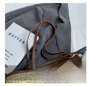 Detail of woven straw tote bag with brown leather handles and decorative pearl leaf charm