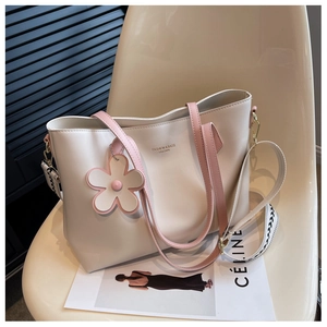 Detail of beige leather tote bag with wide geometric strap and floral pendant charm