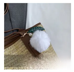 Detail of white faux fur pompom charm with green leaf and pearl on woven tote bag