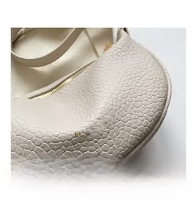 Detail of cream-colored dumpling bag featuring gold logo and pebble leather texture