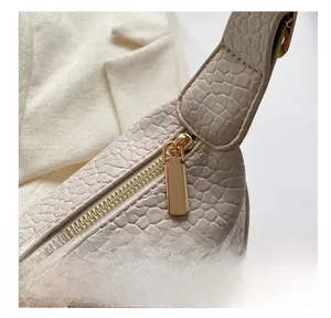 Detailed close-up of smooth gold metal zipper and crocodile embossed texture on beige bag