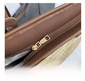 Detail of smooth gold zipper closure on straw woven tote bag with brown leather trim