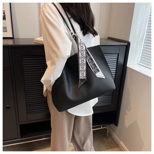 Detail of a large black leather tote bag featuring a decorative silk scarf on the handle