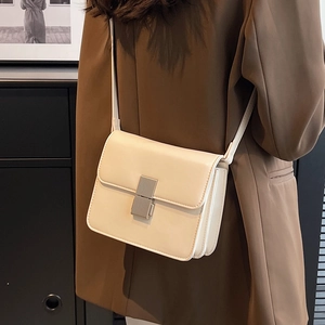 Elegant cream crossbody bag with silver buckle worn over a brown blazer coat