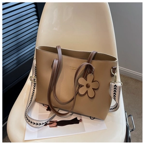 Detail of khaki tote bag with wide arrow pattern strap and leather flower charm