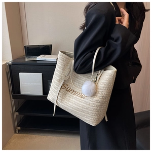 Close-up of straw tote bag with Summer embroidery and a white pompom charm detail