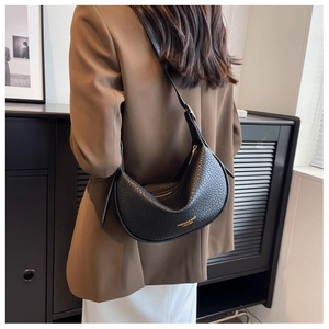 Detail of black pebbled leather crescent bag with adjustable strap worn by model