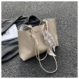 Detail of beige tote bag with litchi texture, drawstring closure, and printed silk scarf