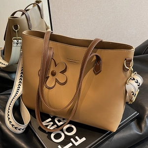 Large khaki tote bag with wide patterned strap and floral charm in a minimalist style