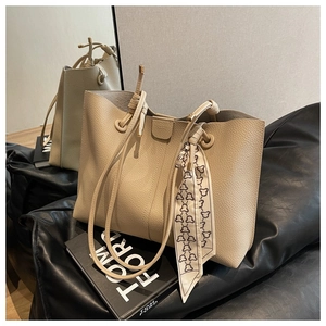 Detail of beige lychee leather tote bag with elegant silk scarf on a black leather seat