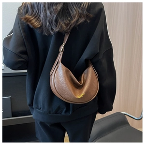 Close-up of brown textured leather crescent bag showing the adjustable strap and gold branding