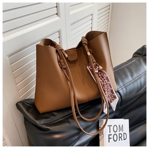 Detail of caramel leather tote bag with silk scarf on a stylish black leather sofa