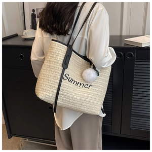 Detail of straw tote bag featuring Summer embroidery, black straps and a white pompom
