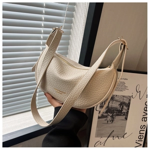 Detail of creamy white textured leather moon bag with golden fashion branding and strap