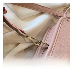 Detail of pink pebbled leather crossbody bag with polished gold metal hardware and stitching