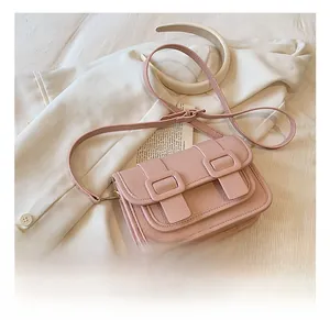 Detail shot of a pink pebbled leather crossbody bag with buckle straps on a white blazer