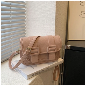 Detail of pink lychee leather crossbody bag with dual straps on a white book base