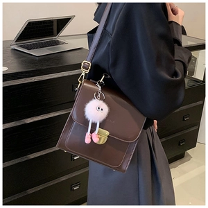 Detailansicht der braunen matten Ledertasche mit Goldschnalle und Plüsch-Anhänger
