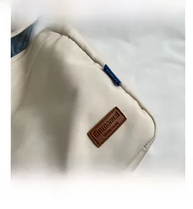 Detail view of cream canvas tote fabric texture with stitched leather Emmanuel logo tag