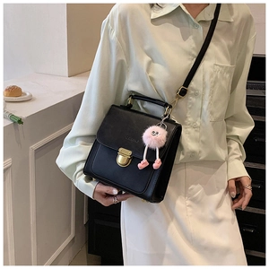 Detail einer schwarzen Ledertasche mit pinkem Plüschanhänger und goldener Schnalle