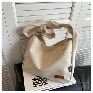Detail of a cream canvas bucket bag featuring a brown leather label and a knotted shoulder strap