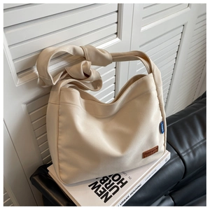 Detailed view of the cream canvas tote with a wide knotted strap and subtle leather brand tag
